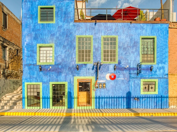 A two-story building with a blue facade, green window frames, and a red umbrella on the roof. - El Andariego (Oaxaca)