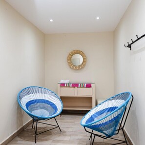 A hallway with two blue woven chairs, a small desk with a mirror, and a coat rack. - El Andariego (Oaxaca)