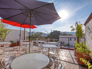 An outdoor patio with tables and chairs, a red umbrella, and potted plants. - El Andariego (Oaxaca)