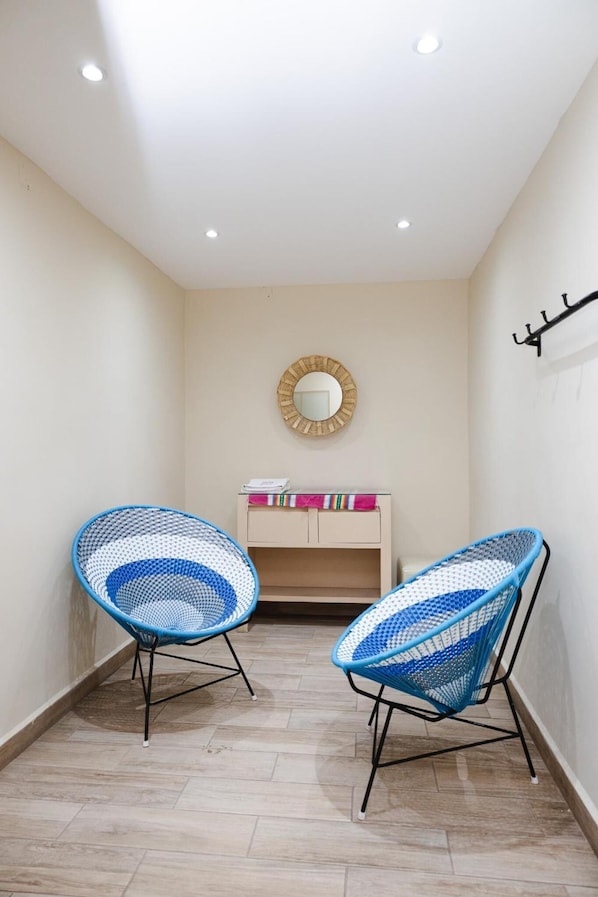 A narrow hallway with two blue wicker chairs, a small vanity with a mirror, and a coat rack. - El Andariego (Oaxaca)