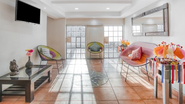 Un salon spacieux avec une table basse en verre, deux fauteuils colorés, un canapé et un téléviseur fixé au mur.