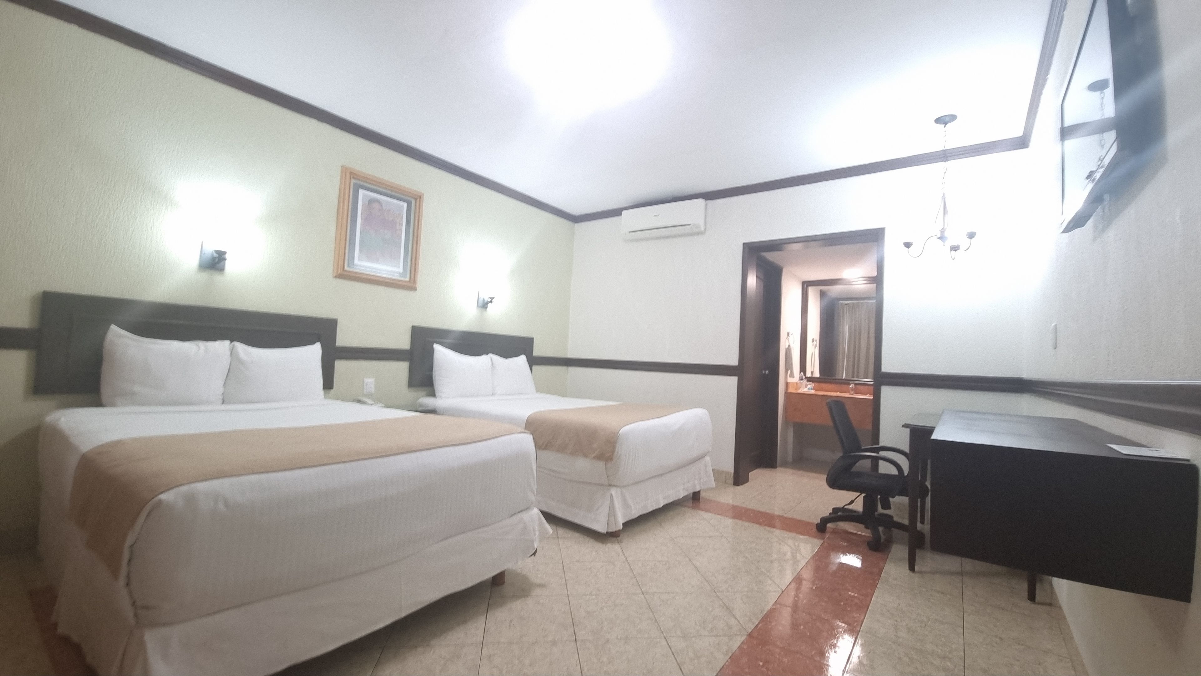 Habitación de hotel con dos camas, un escritorio, una silla, un aire acondicionado y un espejo.