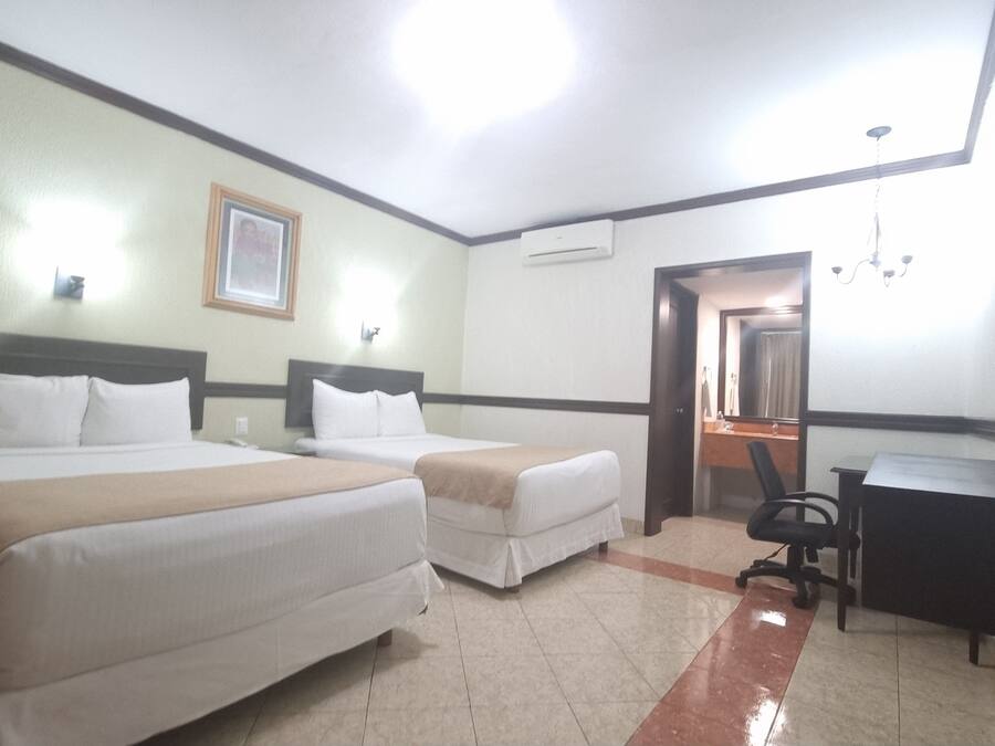 Habitación de hotel con dos camas, un escritorio, una silla, un aire acondicionado y un espejo.