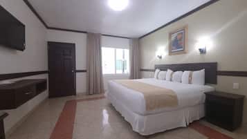 A hotel room with a bed, a nightstand, a TV, a window with curtains, and a painting on the wall.