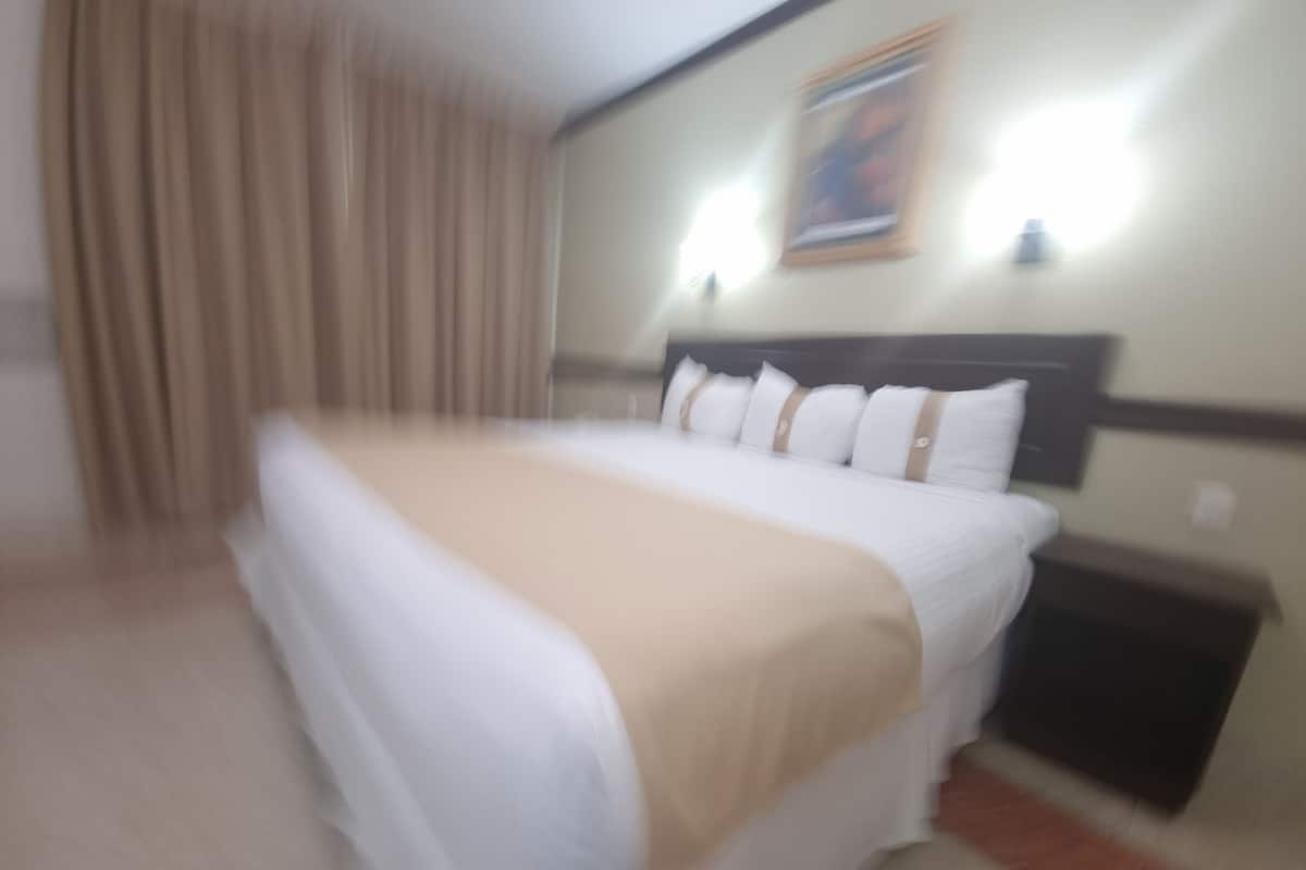 A hotel room with a bed, curtains, a headboard, and a wall-mounted light fixture.