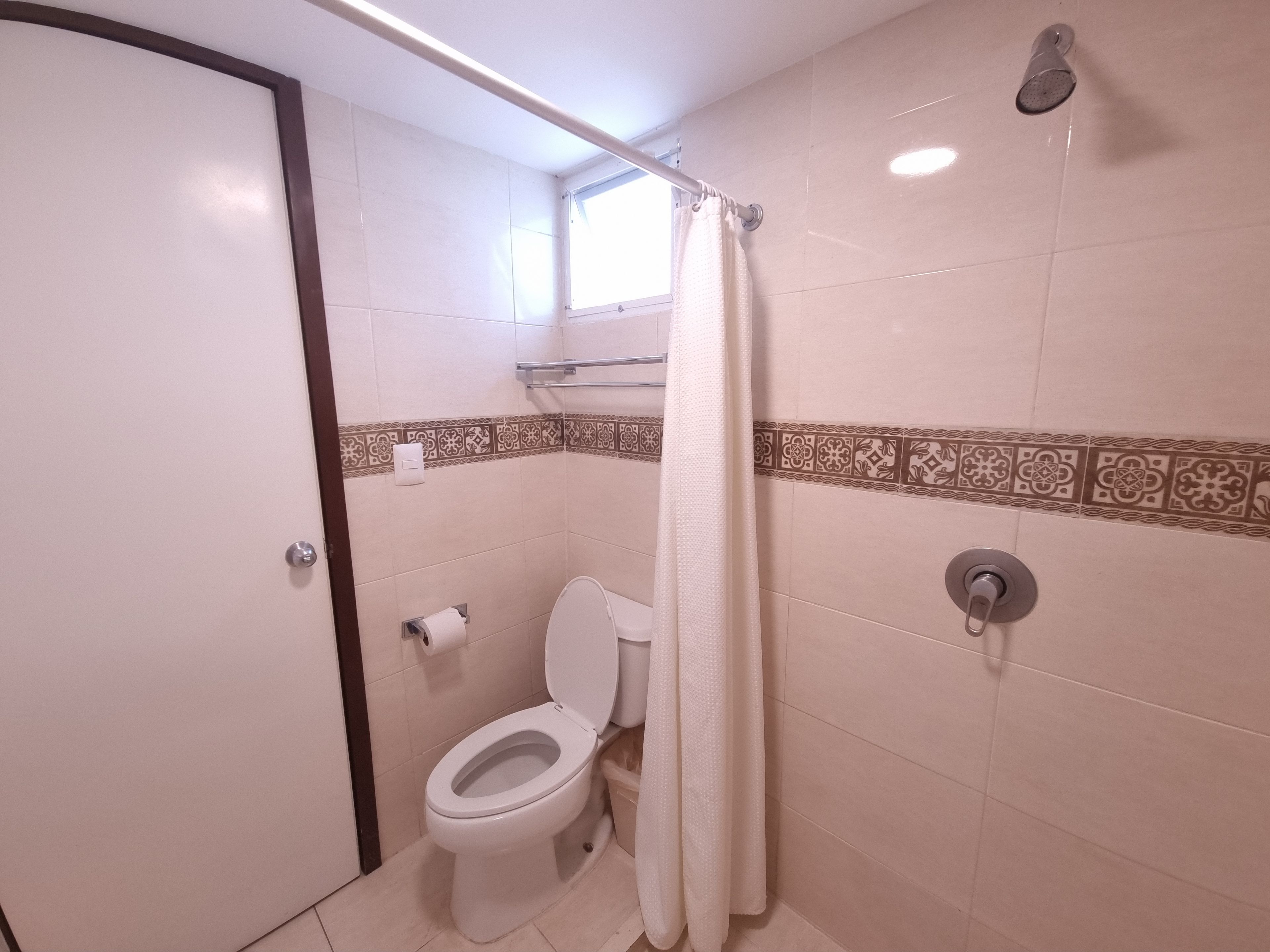 A bathroom with a toilet, a shower, and a towel hanging on a rod.