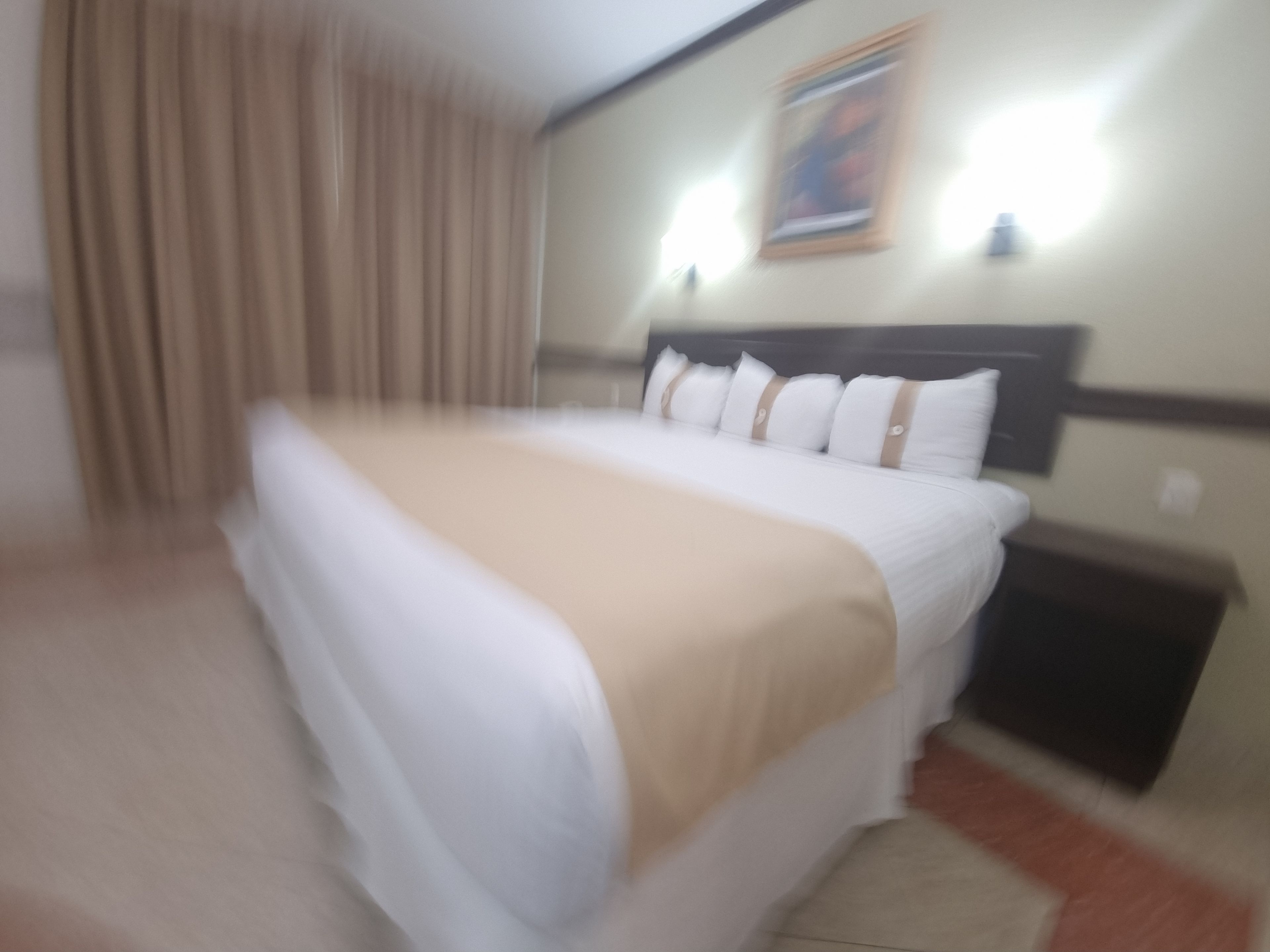 Una habitación de hotel con una cama, cortinas, un cabecero y una lámpara fijada a la pared.