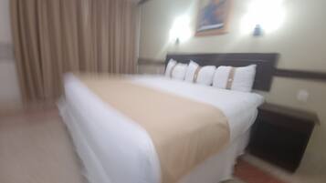 Una habitación de hotel con una cama, cortinas, un cabecero y una lámpara fijada a la pared.