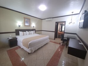 Una habitación de hotel con una cama grande, mesitas de noche, un escritorio, una silla, un equipo de aire acondicionado y un televisor.