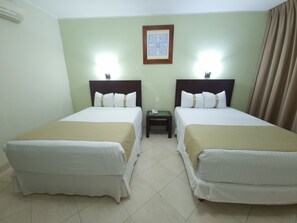 Une chambre d’hôtel avec deux lits simples, une table de chevet avec un téléphone et un tableau encadré au mur.