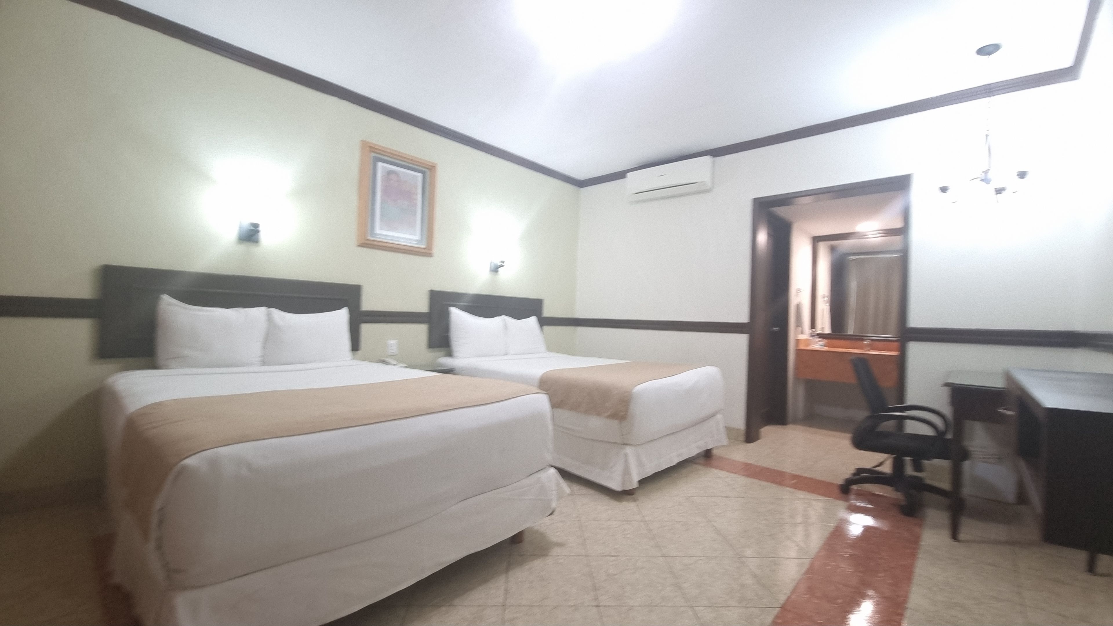 A hotel room with two beds, a desk, a chair, and a mirror.