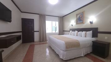 Una habitación de hotel con cama, mesita de noche, televisión y ventana con cortinas.
