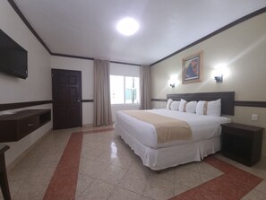 A hotel room with a bed, bedside table, TV, and a window with curtains. - Hotel Casa Blanca (Chetumal)