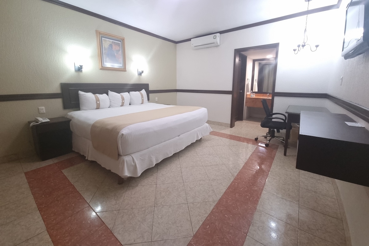 A hotel room with a bed, bedside table, desk, chair, and a mirror.