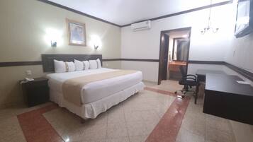 Habitación de hotel con cama, mesita de noche, escritorio, silla y baño visible a través de una puerta abierta.