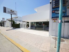 L’entrée d’un hôtel, avec une enseigne indiquant « Casa Blanca », une porte d’entrée et un distributeur automatique de billets visible sur le trottoir.