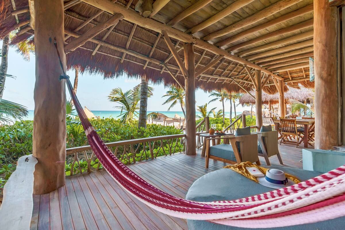 A wooden deck with a hammock, chairs, and a table with a hat and book.