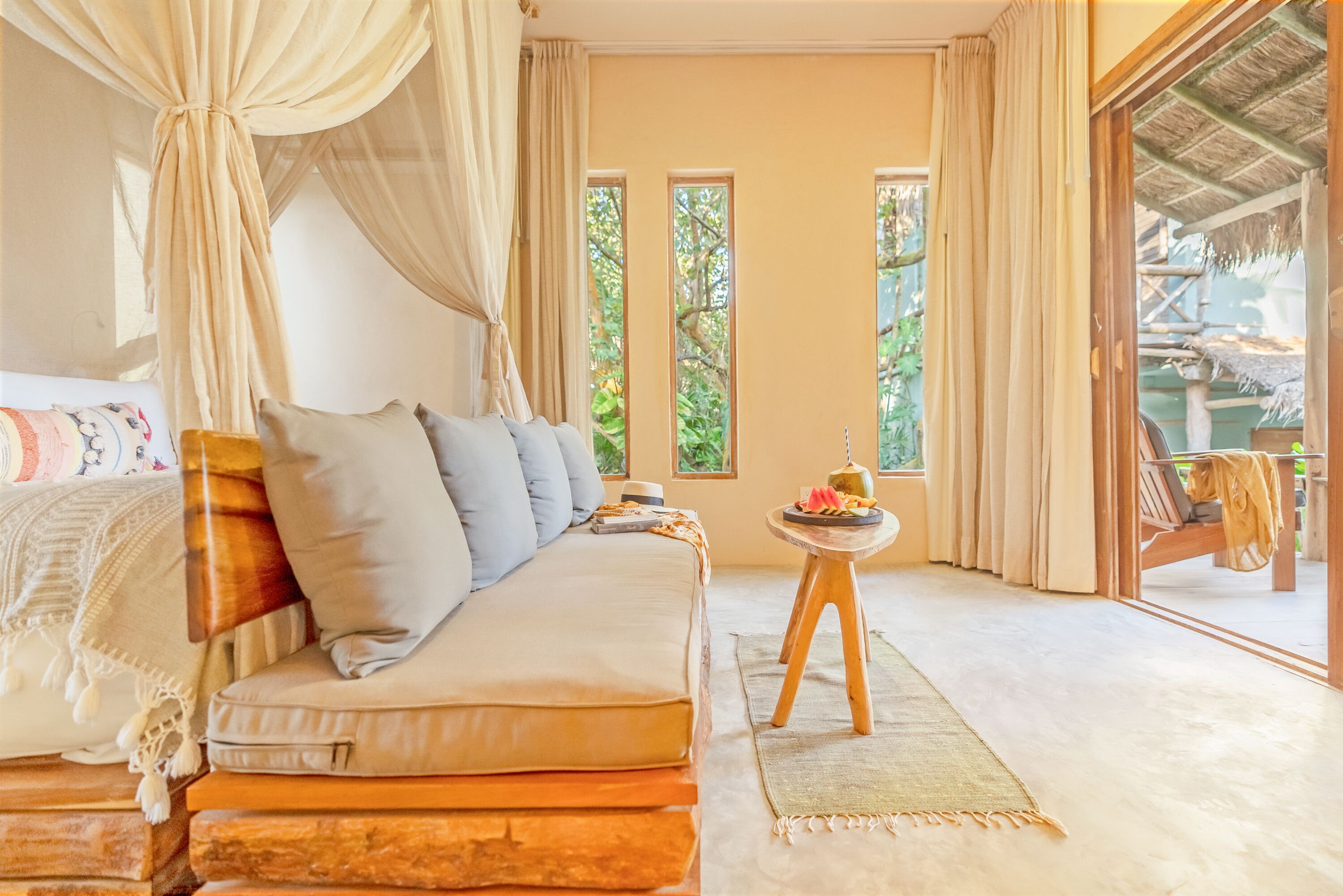 A bedroom with a bed, a sofa, a small table, and a view of the outdoors.