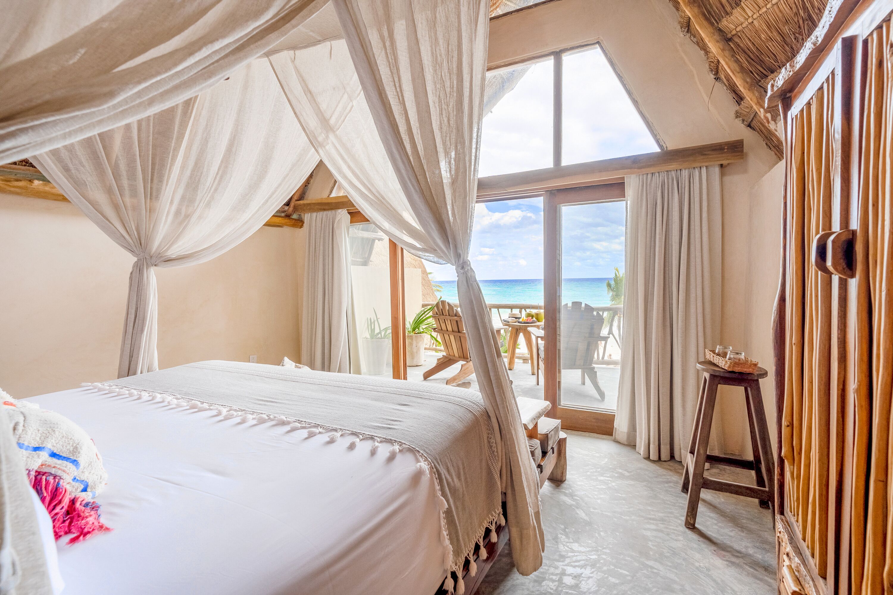 Quarto com cama, varanda vista para o mar e uma cadeira de madeira.
