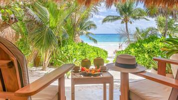 A wooden table with a hat and a plate of food, overlooking a beach with palm trees and the ocean.