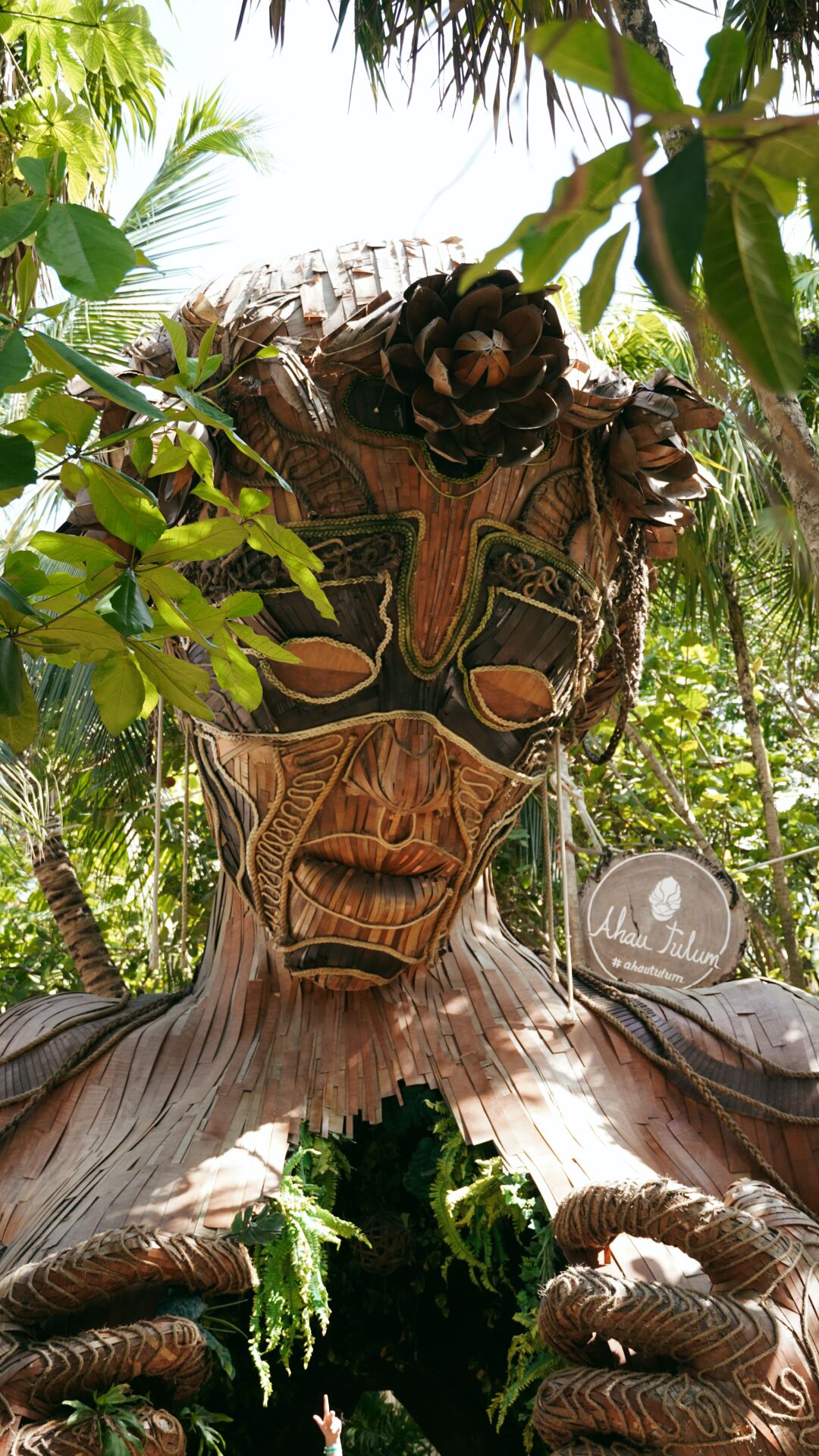 Une grande sculpture en bois, ornée de motifs complexes, entourée d’une végétation luxuriante.