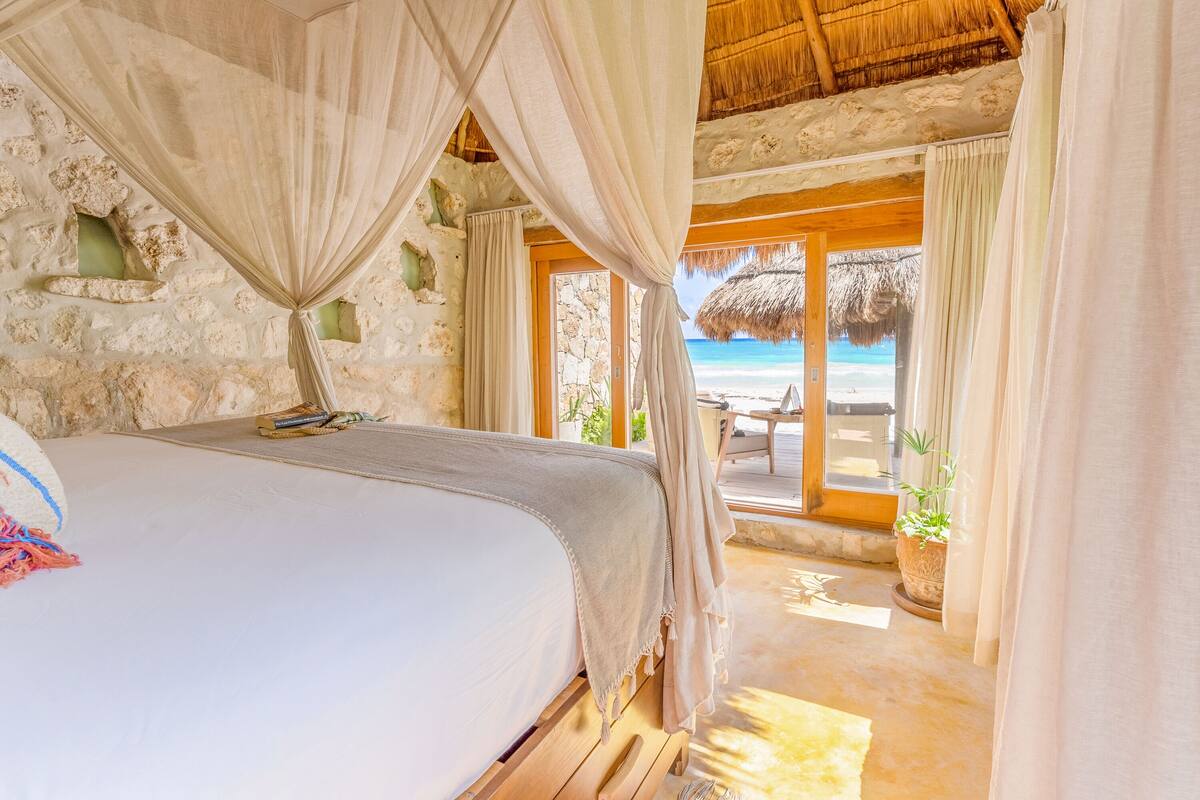 A bedroom with a bed, a mosquito net, and a view of the beach.
