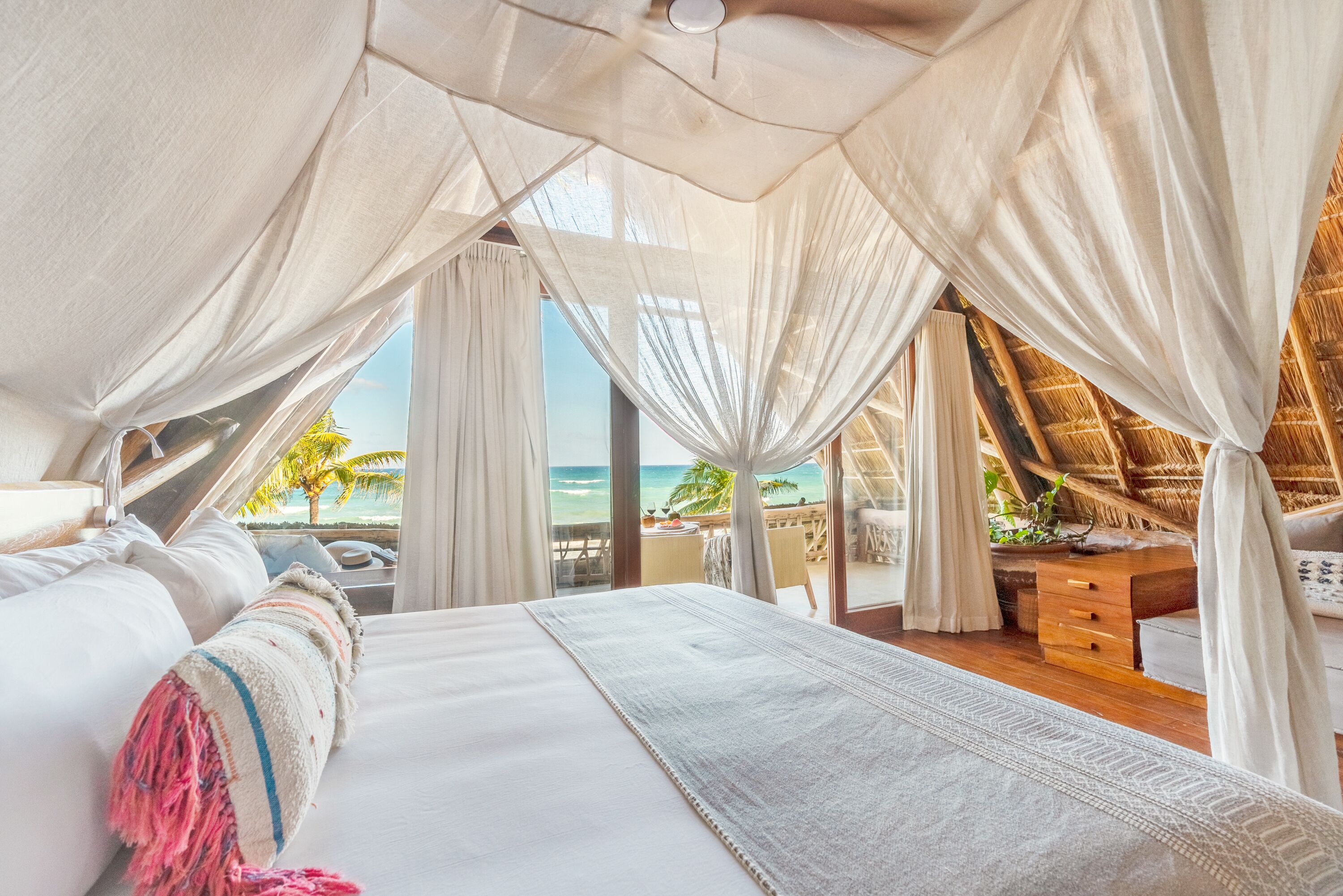 Une chambre avec un grand lit, des rideaux blancs et une vue sur la plage.