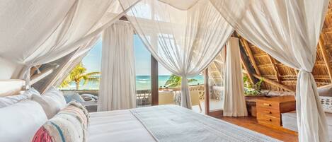 Une chambre avec un grand lit, des rideaux blancs et une vue sur la plage.
