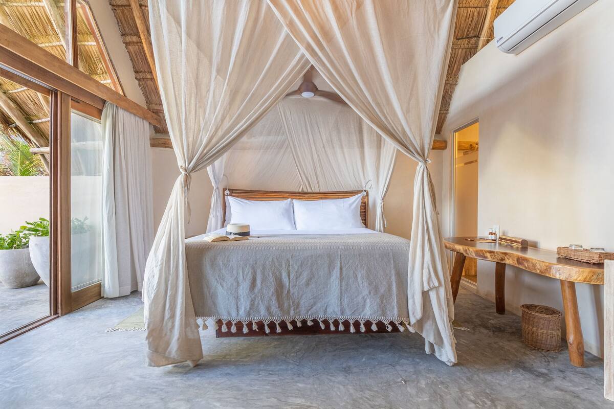A bedroom with a canopy bed, a wooden table, and a view of the outdoors.