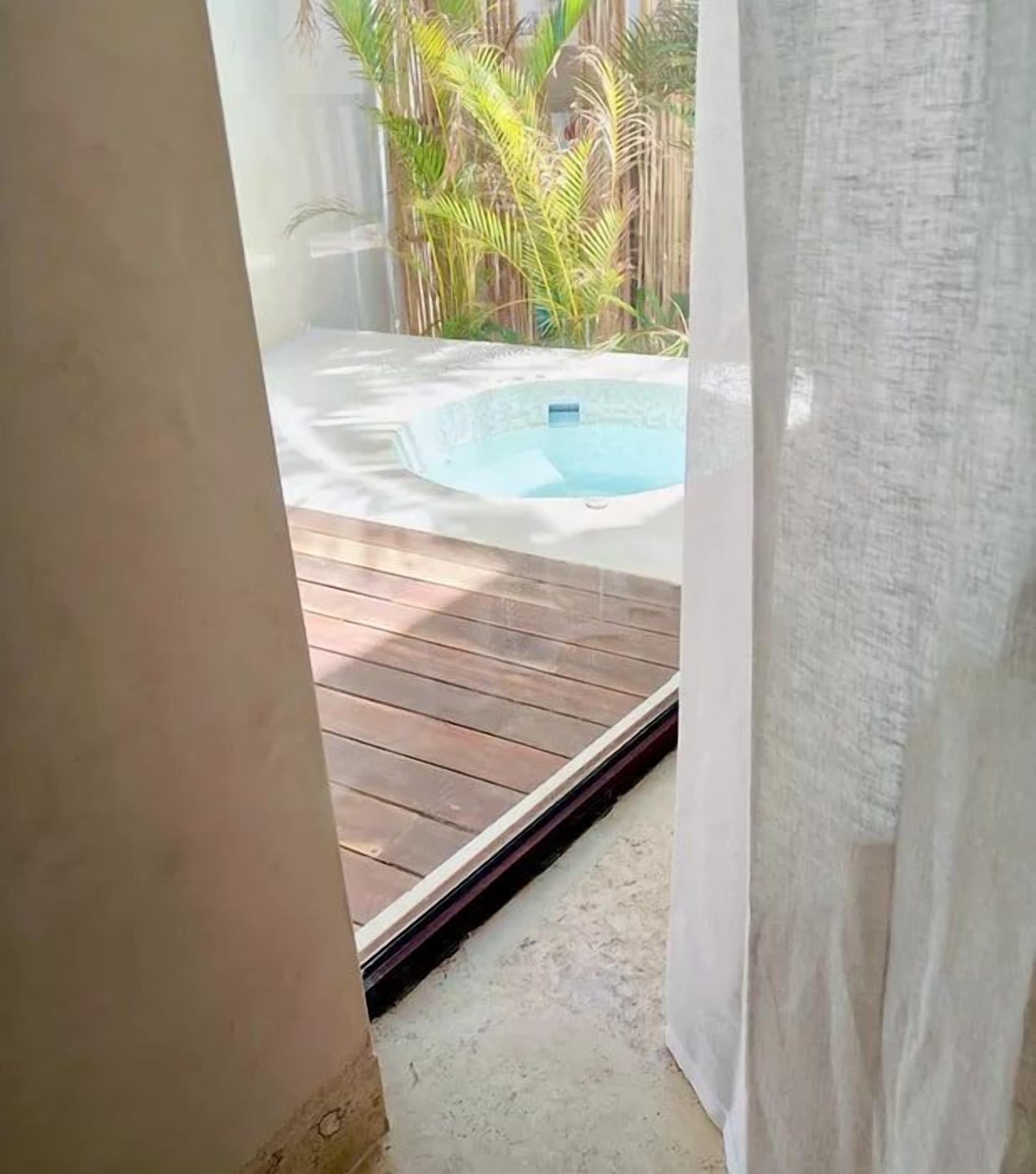 A view of a wooden deck leading to a hot tub surrounded by tropical plants.