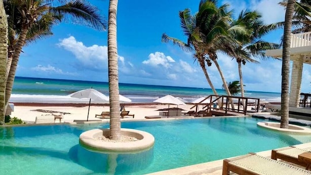A pool area with lounge chairs and umbrellas, palm trees, and a view of the beach and ocean. - Azucar Hotel Tulum    (Tulum)