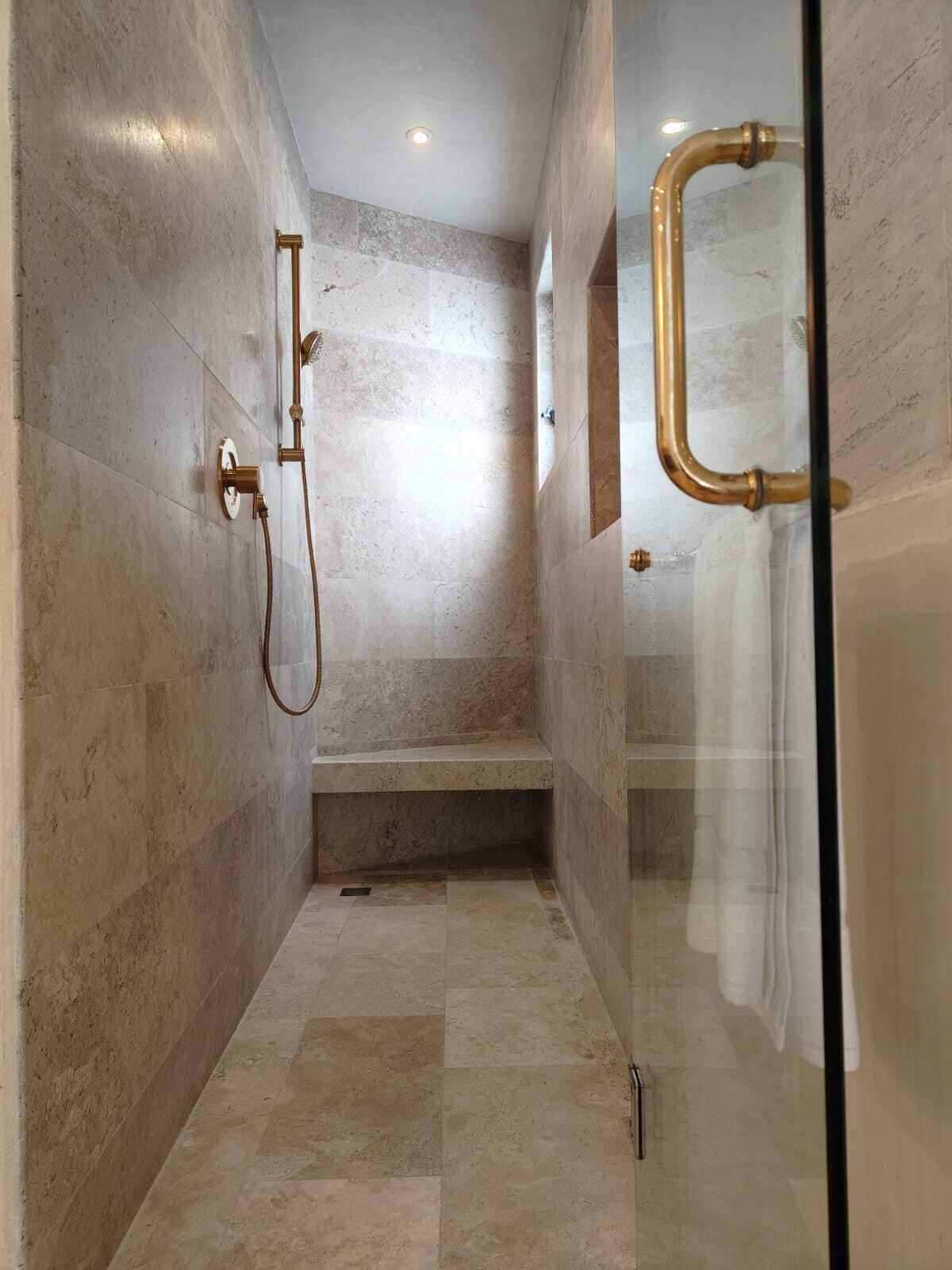 Un espace douche moderne doté d’une porte en verre, d’un banc et d’un pommeau de douche fixé au mur.