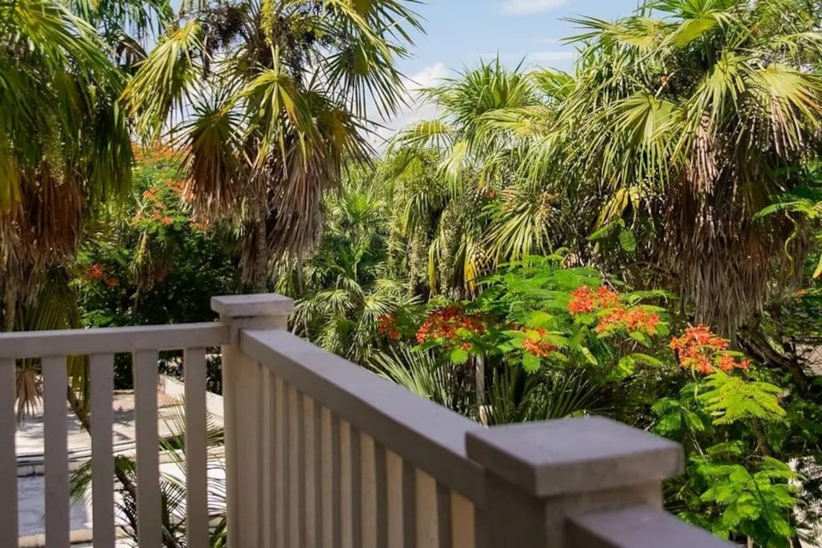 Varanda com guarda-corpo branco, com vista para um jardim exuberante com diversas plantas e flores.