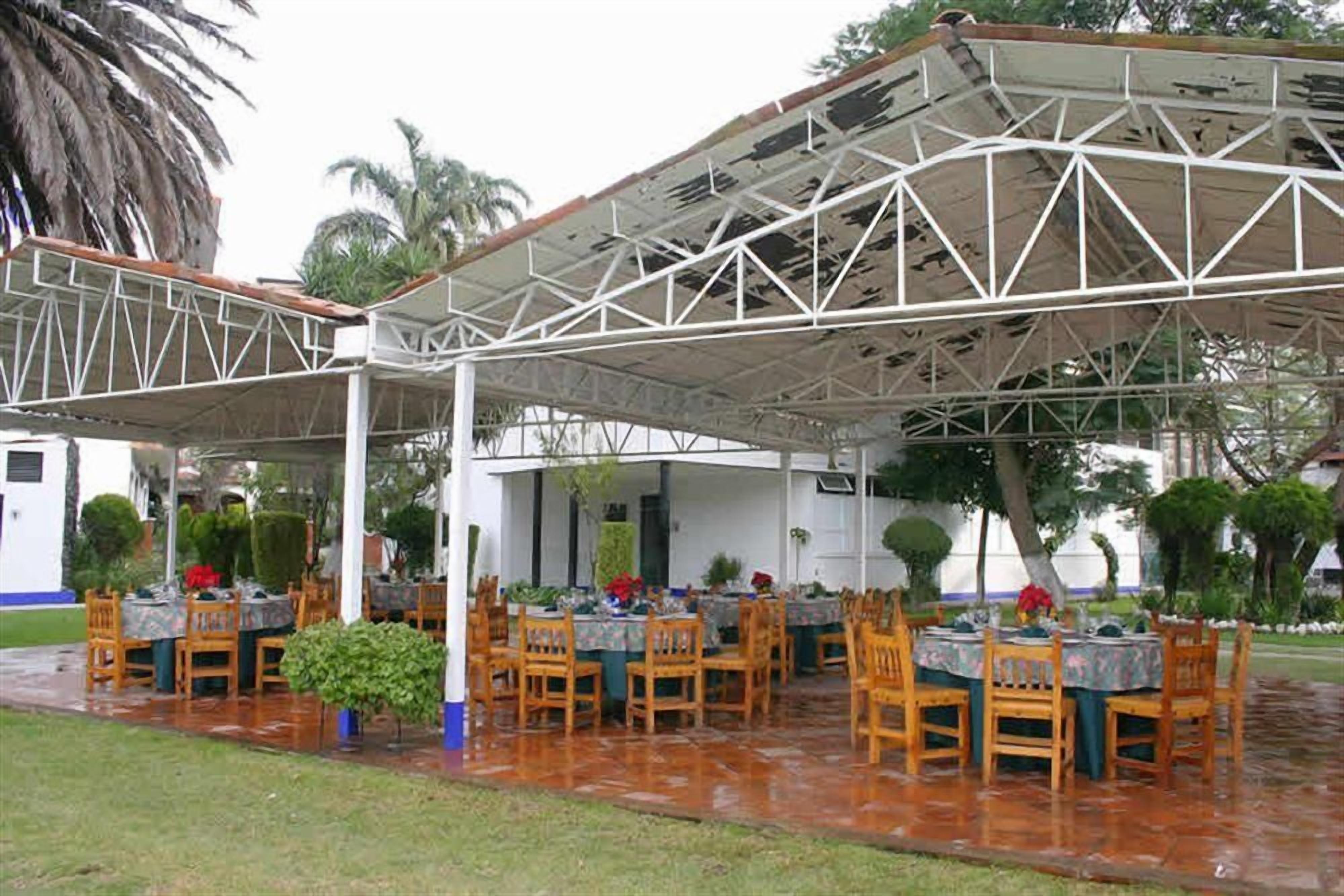 An outdoor dining area with tables and chairs, covered by a metal roof structure.