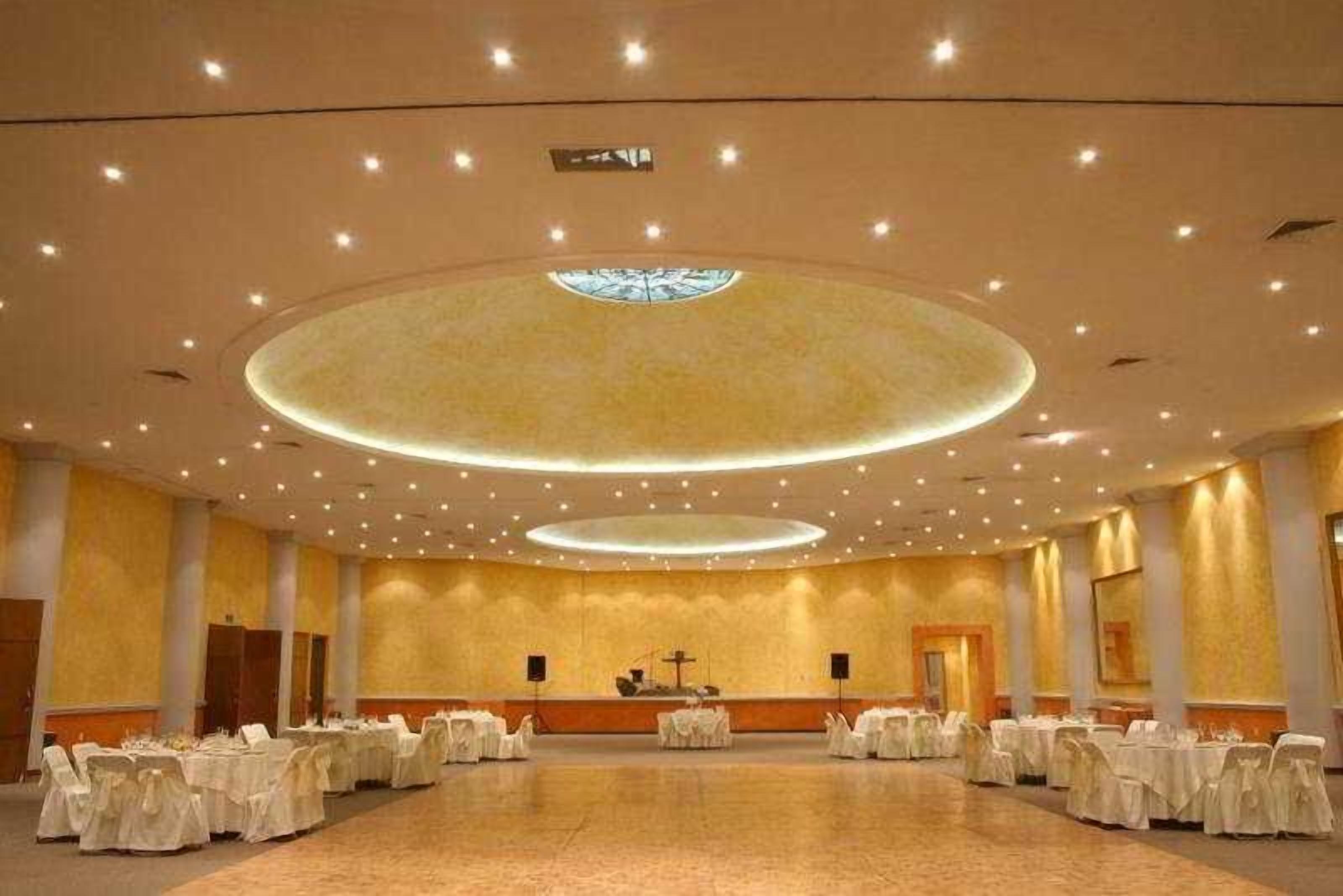 A large hall with round tables and chairs, a central altar, and a circular ceiling design.