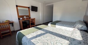 A hotel room with a desk, a mirror, a television, two beds with floral bedding, and a small table with fruits and a glass. - Hotel GS Jerocs Tlaxcala (Tlaxcala)