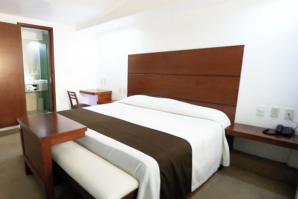 A hotel room with a bed, bedside table, chair, and a small desk with a telephone.
