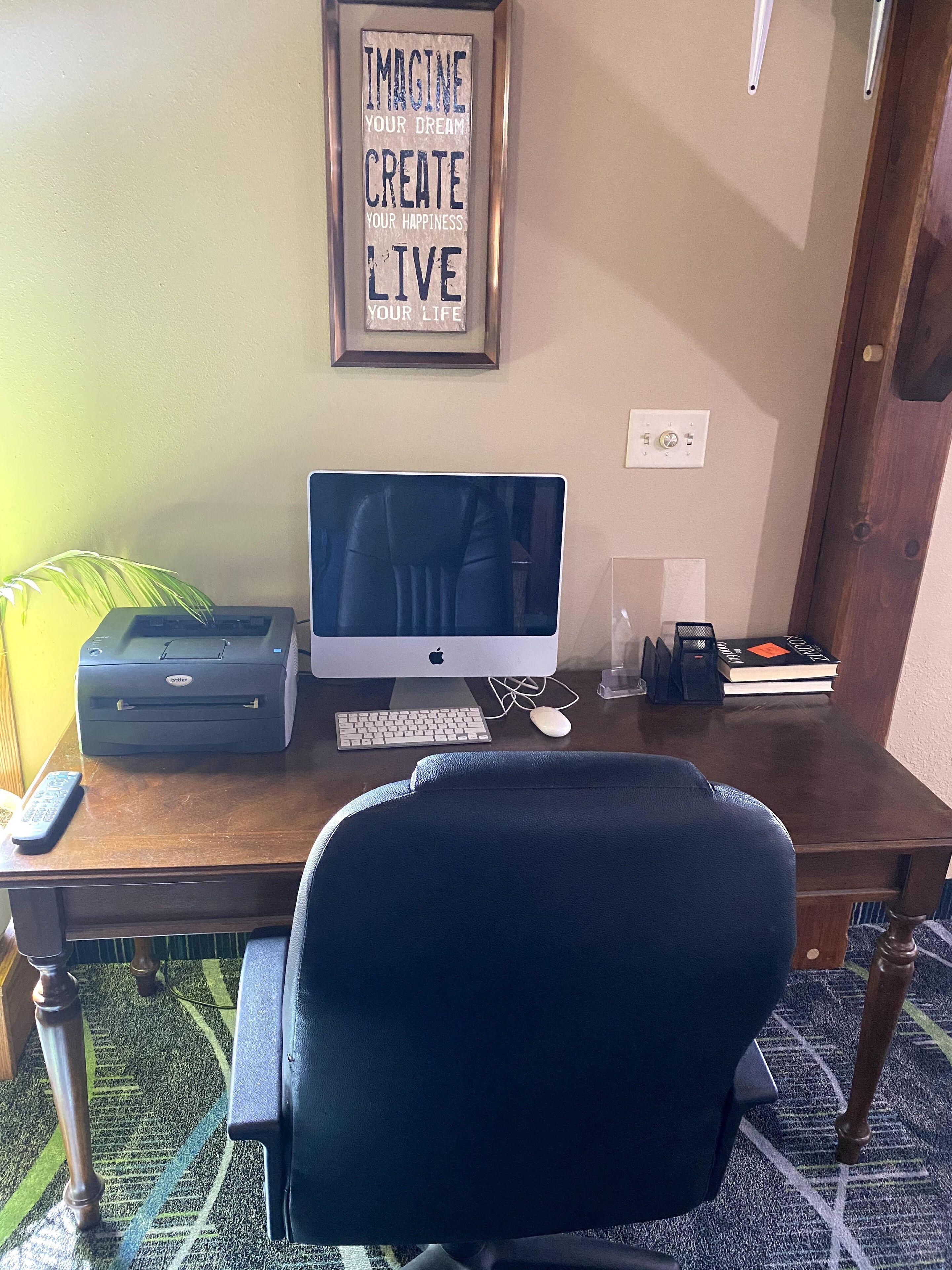 A home office setup with a desk, a computer, a printer, a keyboard, a mouse, a chair, a framed motivational quote, a lamp, and a bookshelf with books.