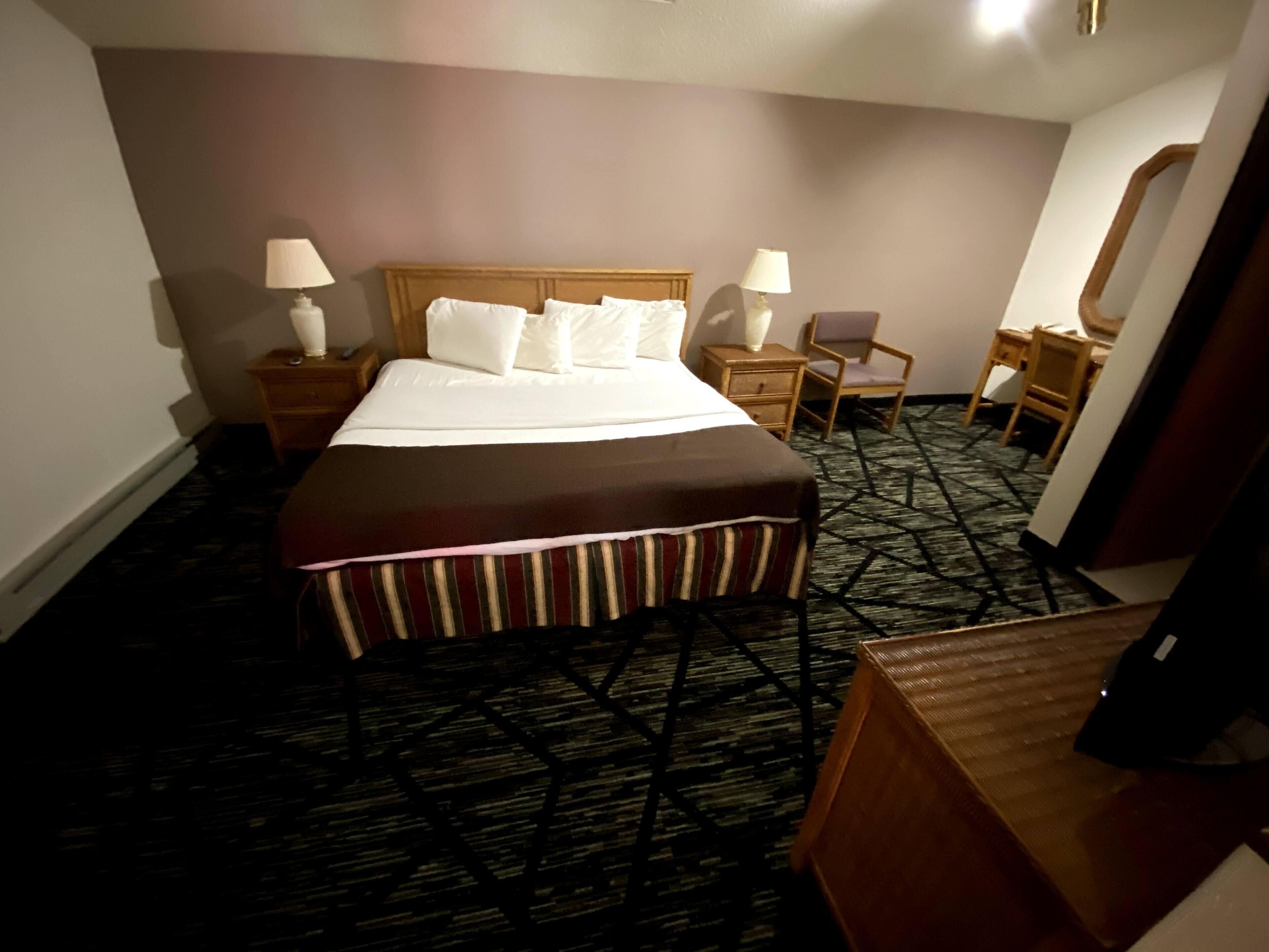 A hotel room with a large bed, two bedside tables with lamps, a chair, a desk, and a mirror.
