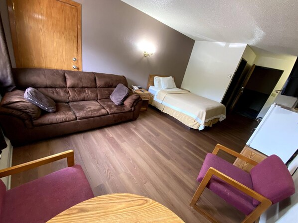 Une pièce de taille modeste, avec un canapé marron, un lit, une petite table en bois et une chaise violette.