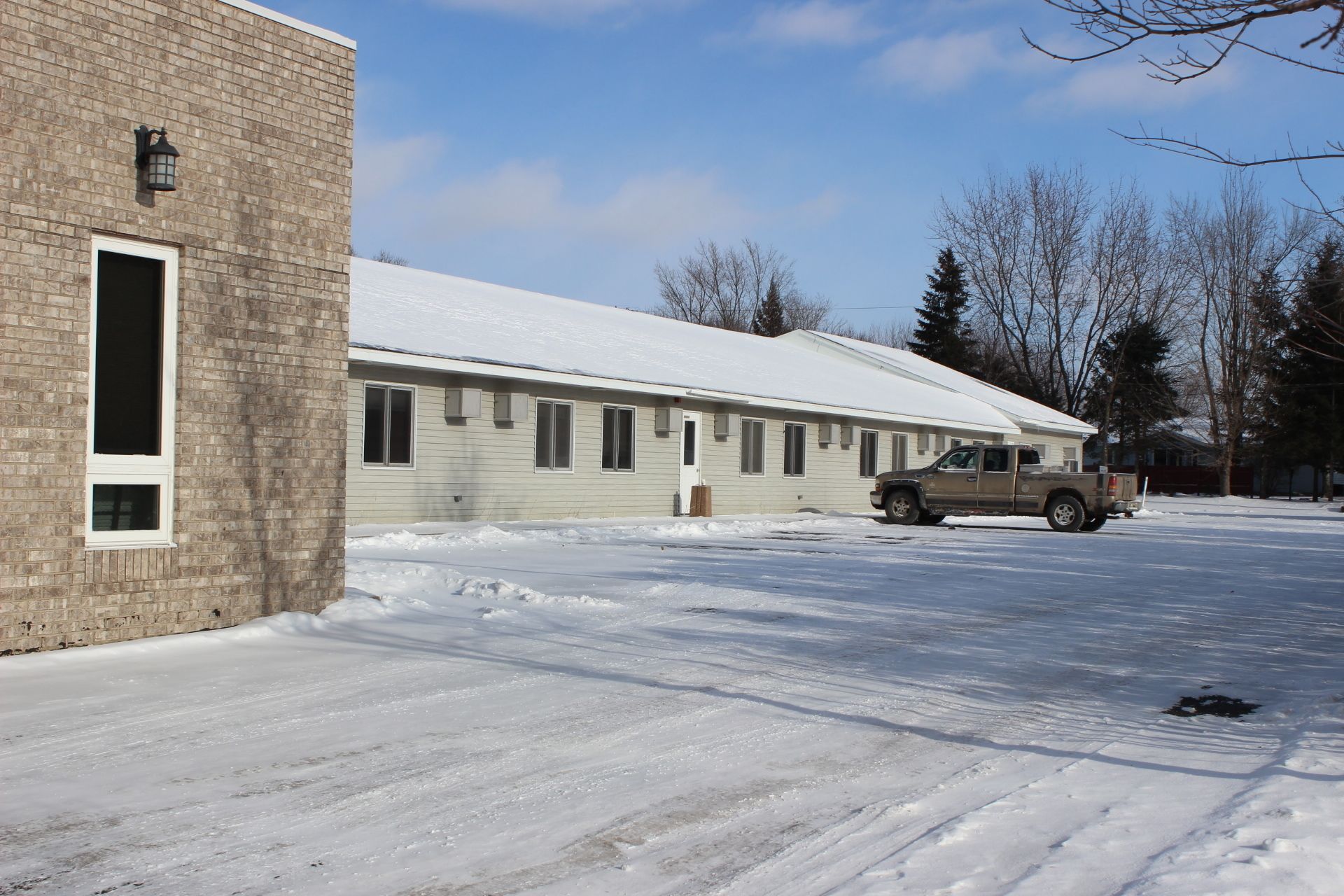 A single-story building with a snow-covered roof and a parked truck in front.