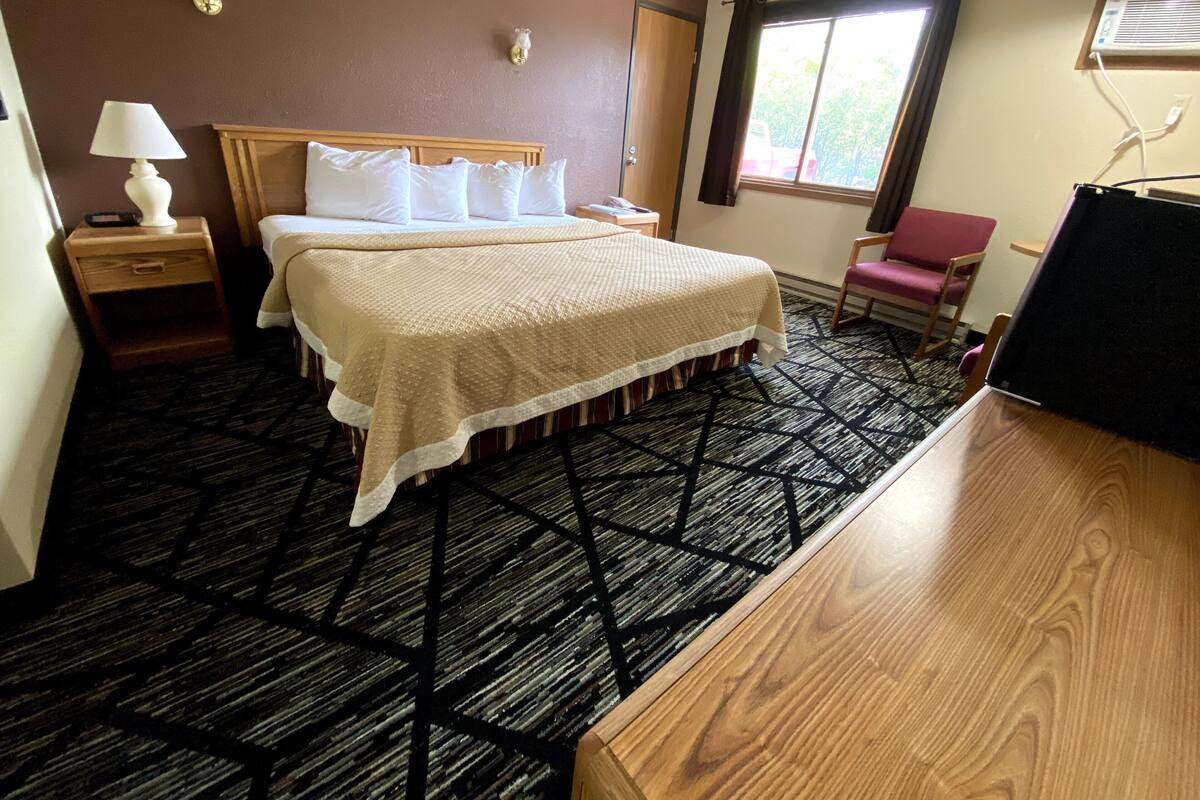 A hotel room with a bed, a nightstand, a desk, a chair, a window, and a wall-mounted air conditioner.