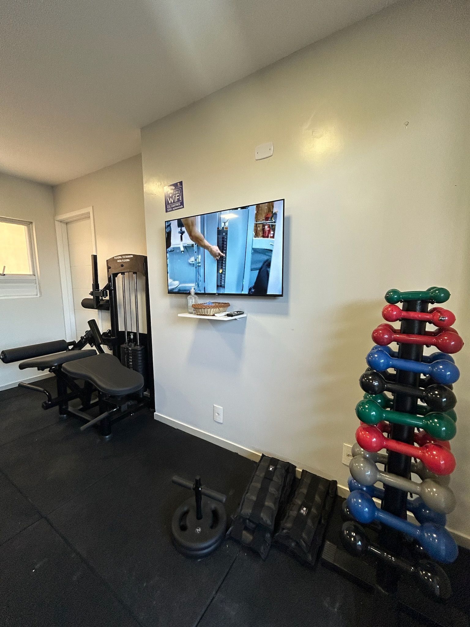 A home gym with exercise equipment, a television mounted on the wall, and a rack of dumbbells.