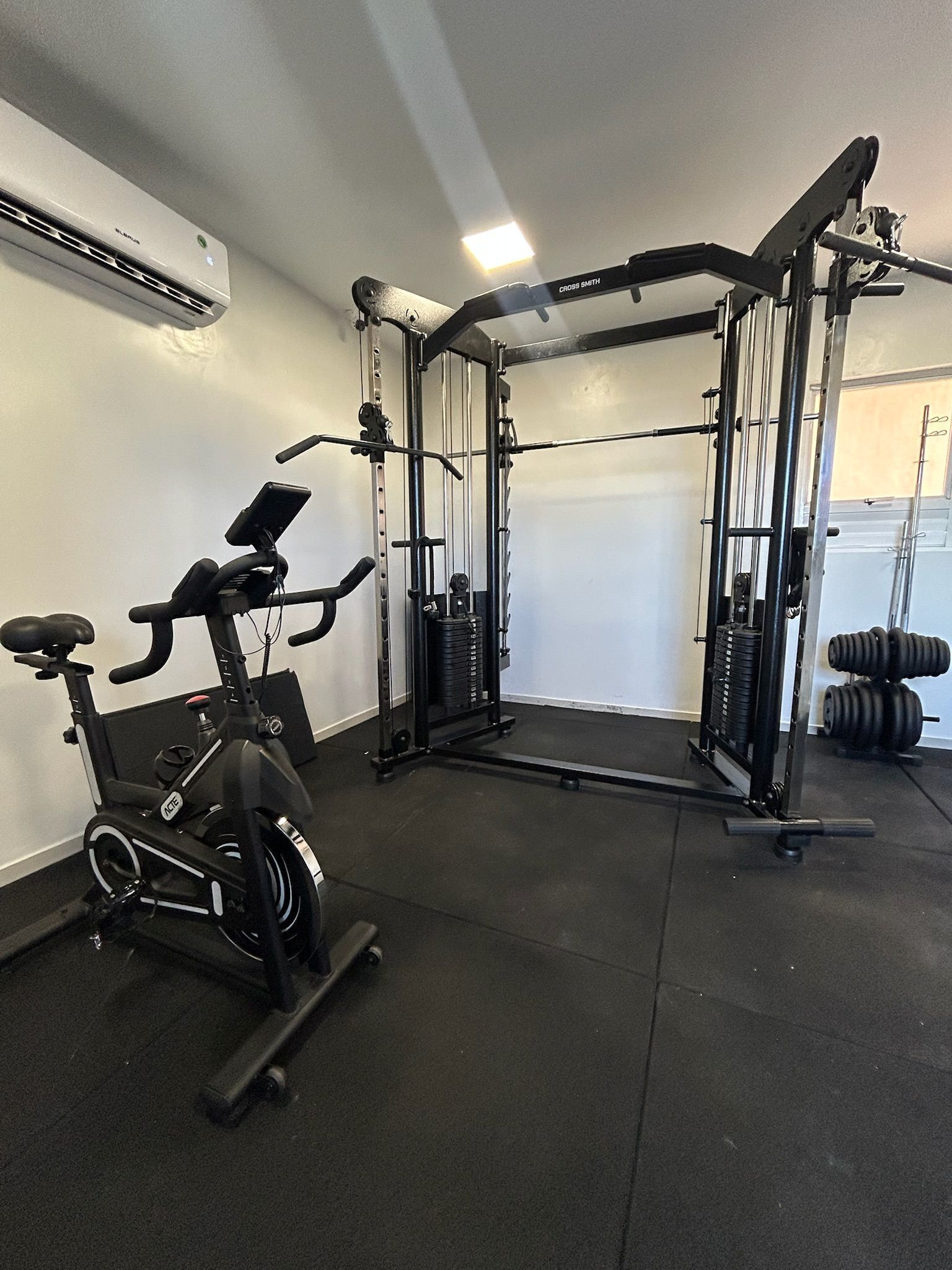 Un gimnasio con bicicleta estática, banco de pesas y pesas sueltas.