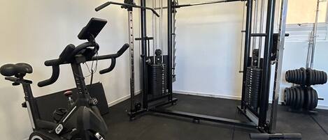 Un gimnasio con bicicleta estática, banco de pesas y pesas sueltas.
