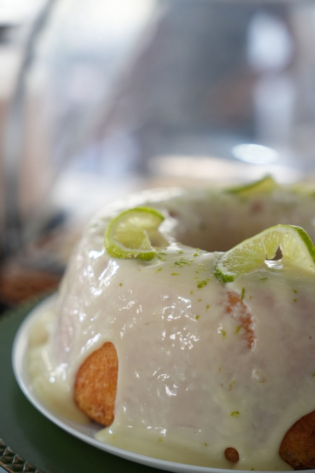 Un dessert con una copertura bianca e cremosa, guarnito con fette di lime e erbe aromatiche, servito su un piatto bianco.