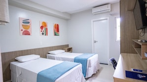 Una habitación de hotel con dos camas, un escritorio, un televisor y obras de arte en la pared.