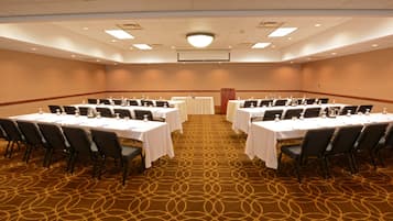 A conference room with multiple tables and chairs, arranged in rows, with a carpeted floor and a ceiling with recessed lighting.