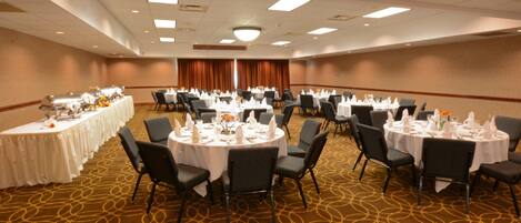 A banquet hall with multiple round tables set for dining, arranged in rows with chairs.