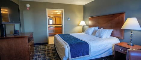 A hotel room with a bed, a desk, a dresser, a lamp, and a bathroom visible through an open door.